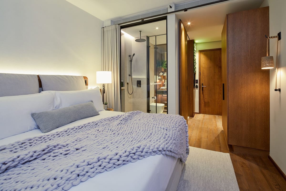 A modern hotel room with a large bed, a glass shower enclosure, and a wooden wardrobe.