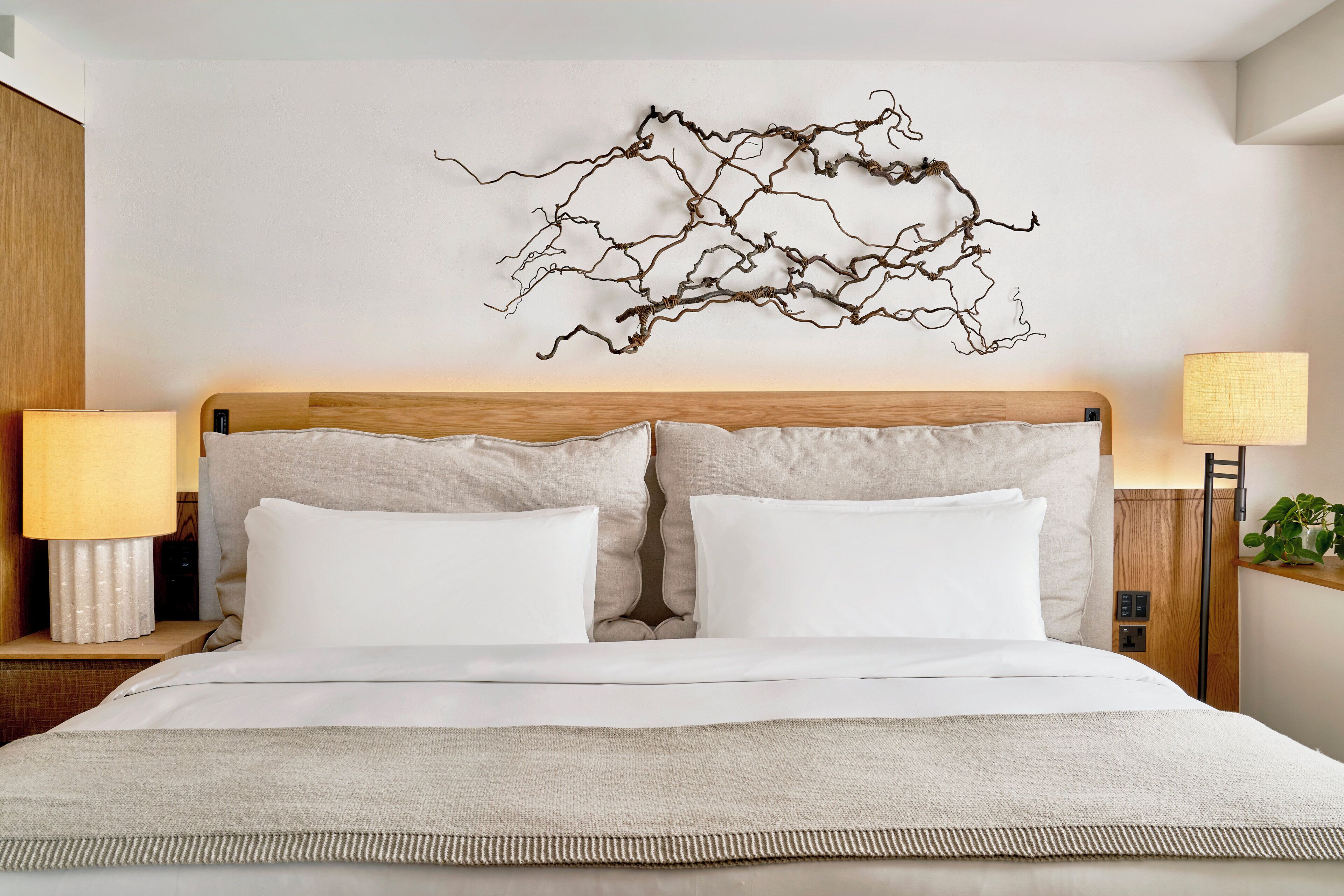 A neatly made bed with white linens, a wooden headboard, and a wall-mounted abstract art piece.