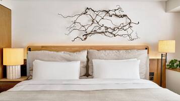 A neatly made bed with white linens, a wooden headboard, and a wall-mounted abstract art piece.