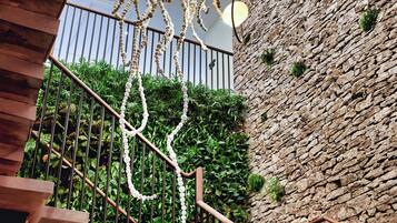 Escada com degraus de madeira e corrimãos de metal, que sobe até um muro de pedra com vegetação.