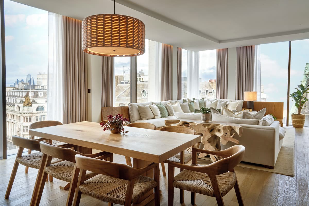 A spacious living area with a wooden dining table, comfortable seating, and a large window offering a city view.