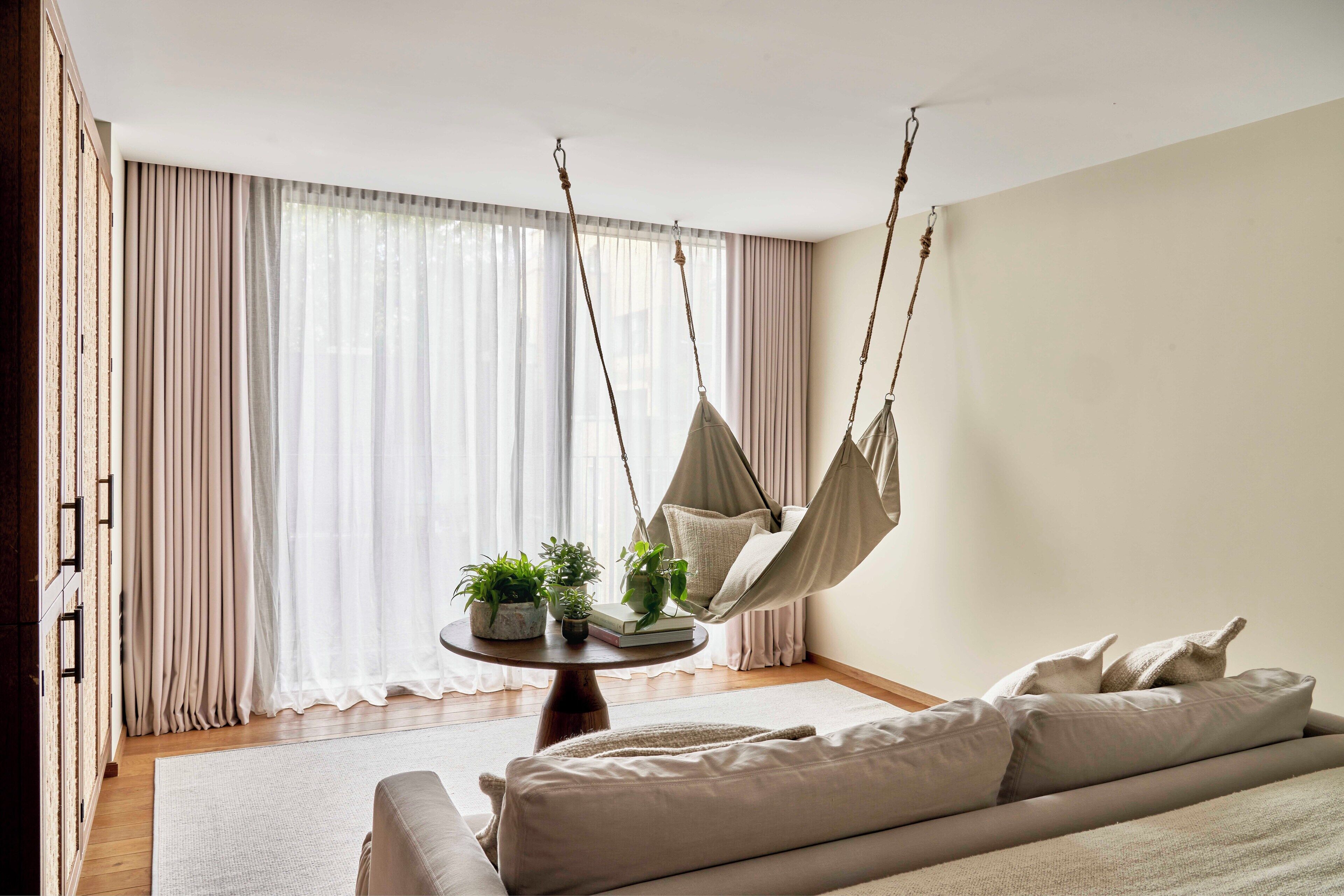 A bedroom with a hanging chair, a round table with plants, and a sofa.