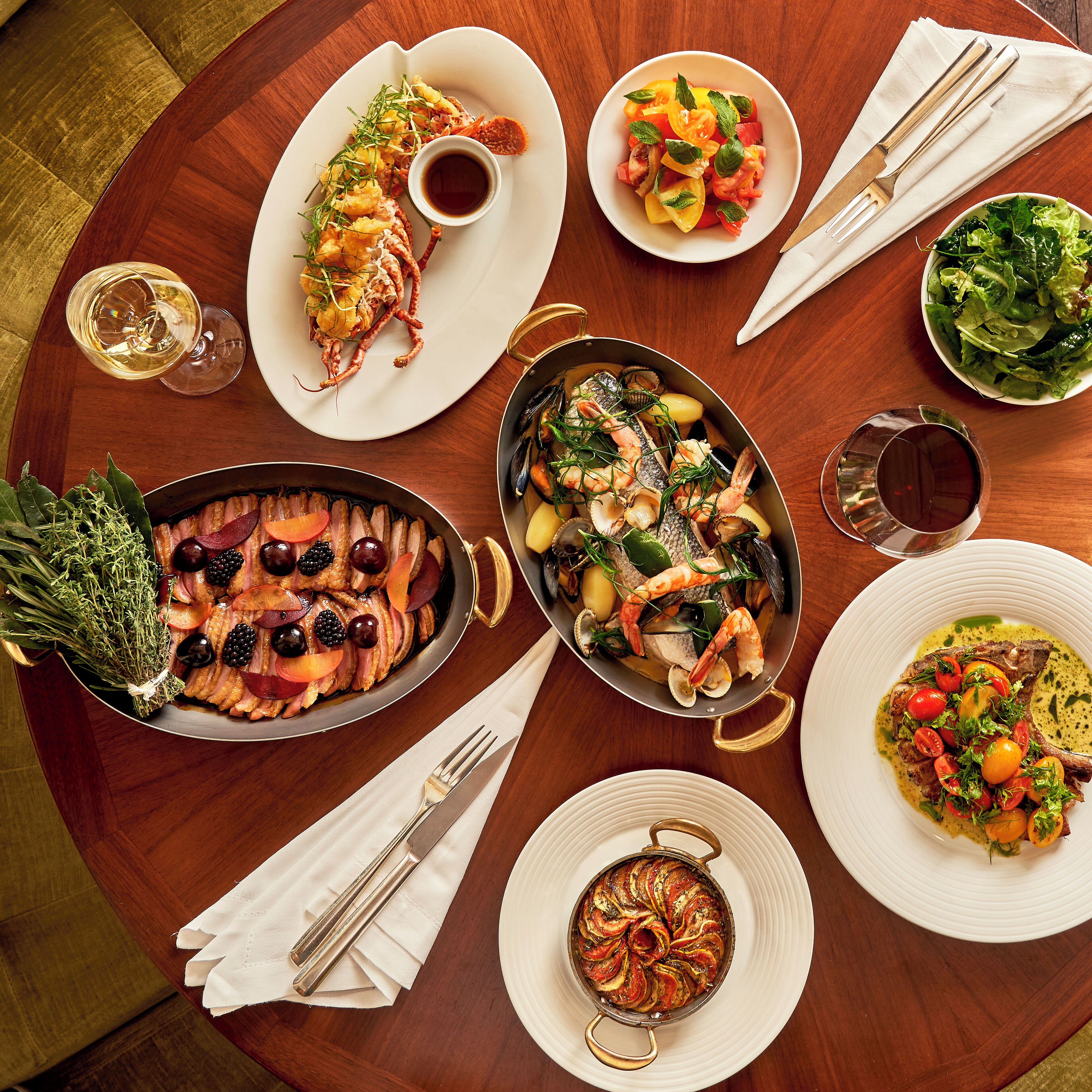 A round wooden table with various dishes, including seafood, salads, and a baked dish, suggesting a meal setting.