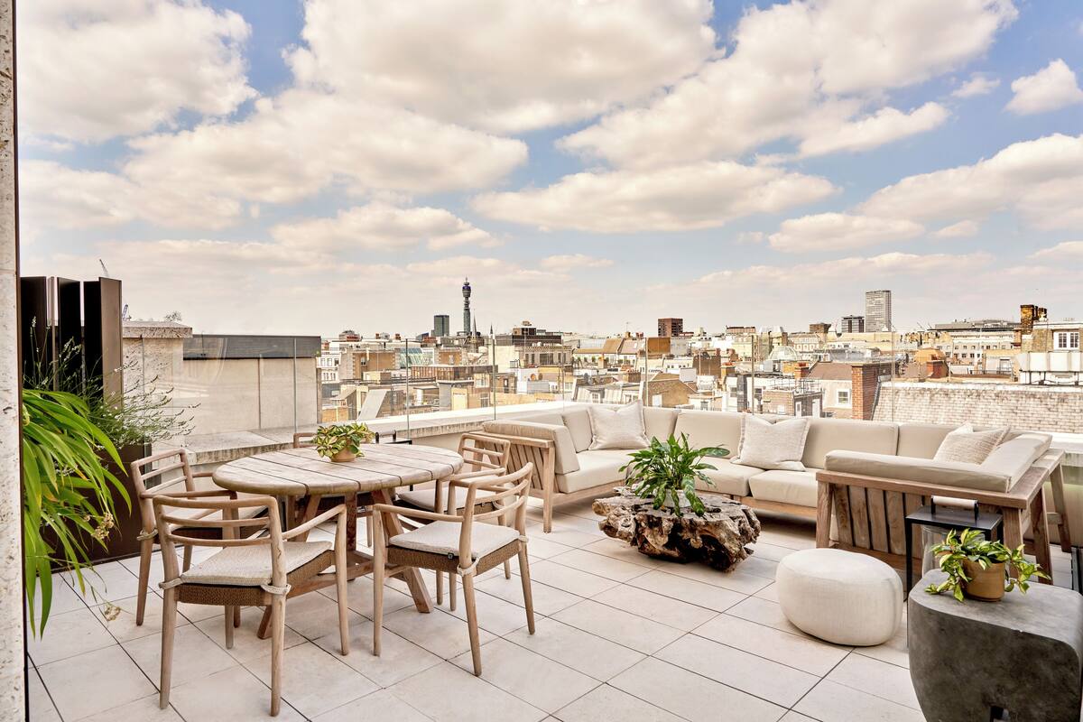 A rooftop terrace with a city view, furnished with a sofa, chairs, and a table.
