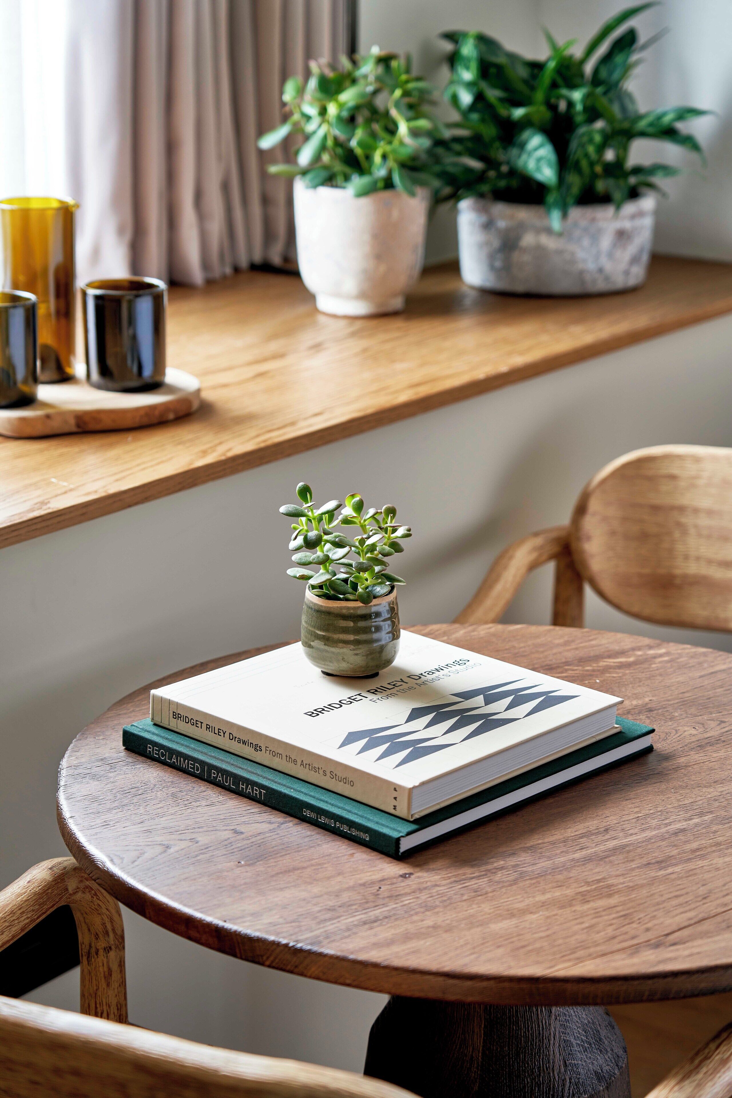 A round wooden table with a book titled "BRIDGET RILEY DRAWINGS" and a small potted plant on it.
