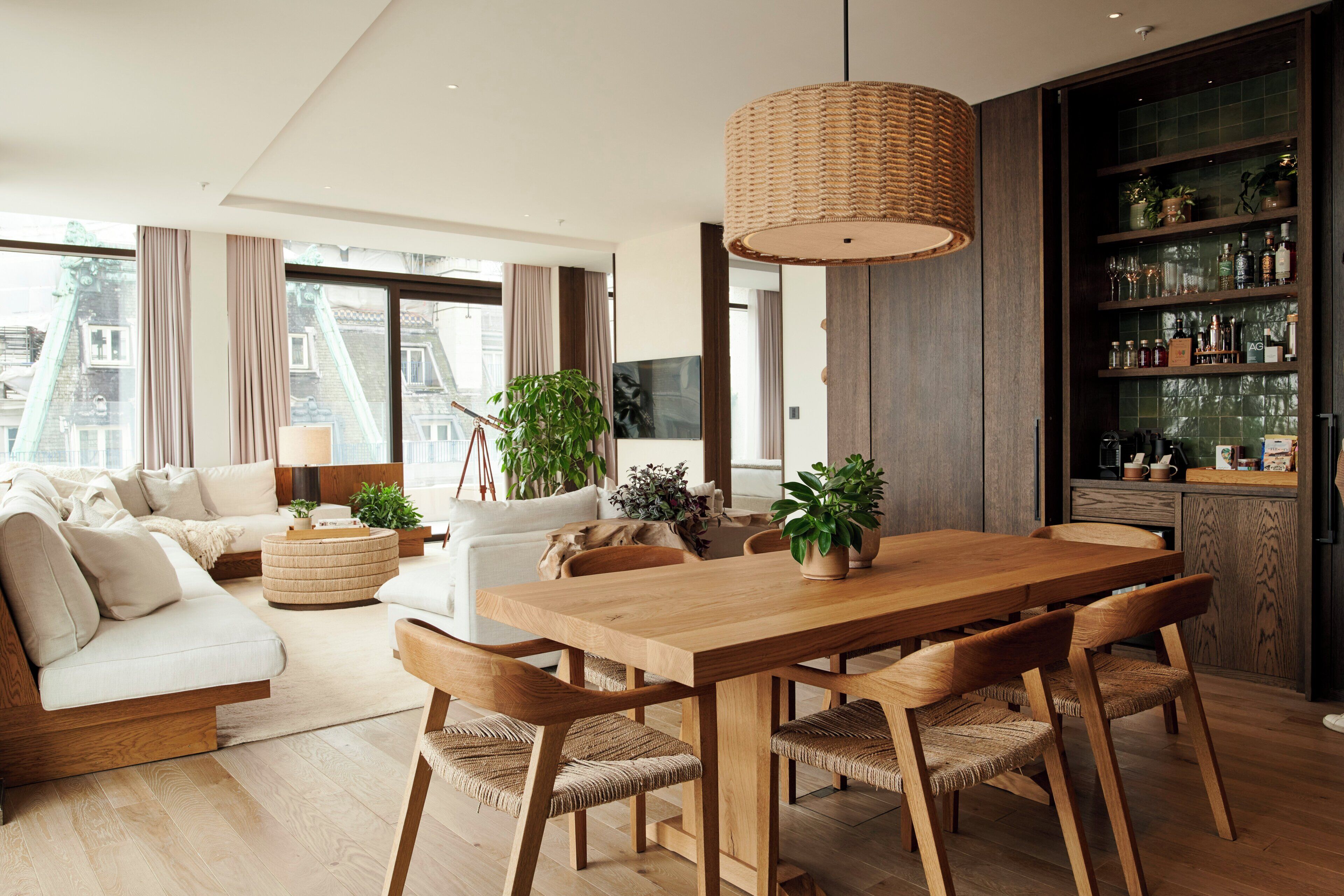 A modern living room with a wooden dining table, woven chairs, and a large woven pendant light.