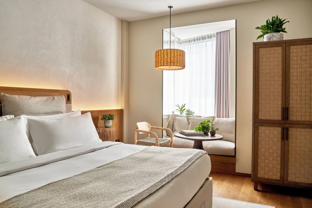 A hotel room with a bed, a sofa, a small table, a chair, a cabinet, and a hanging light fixture.