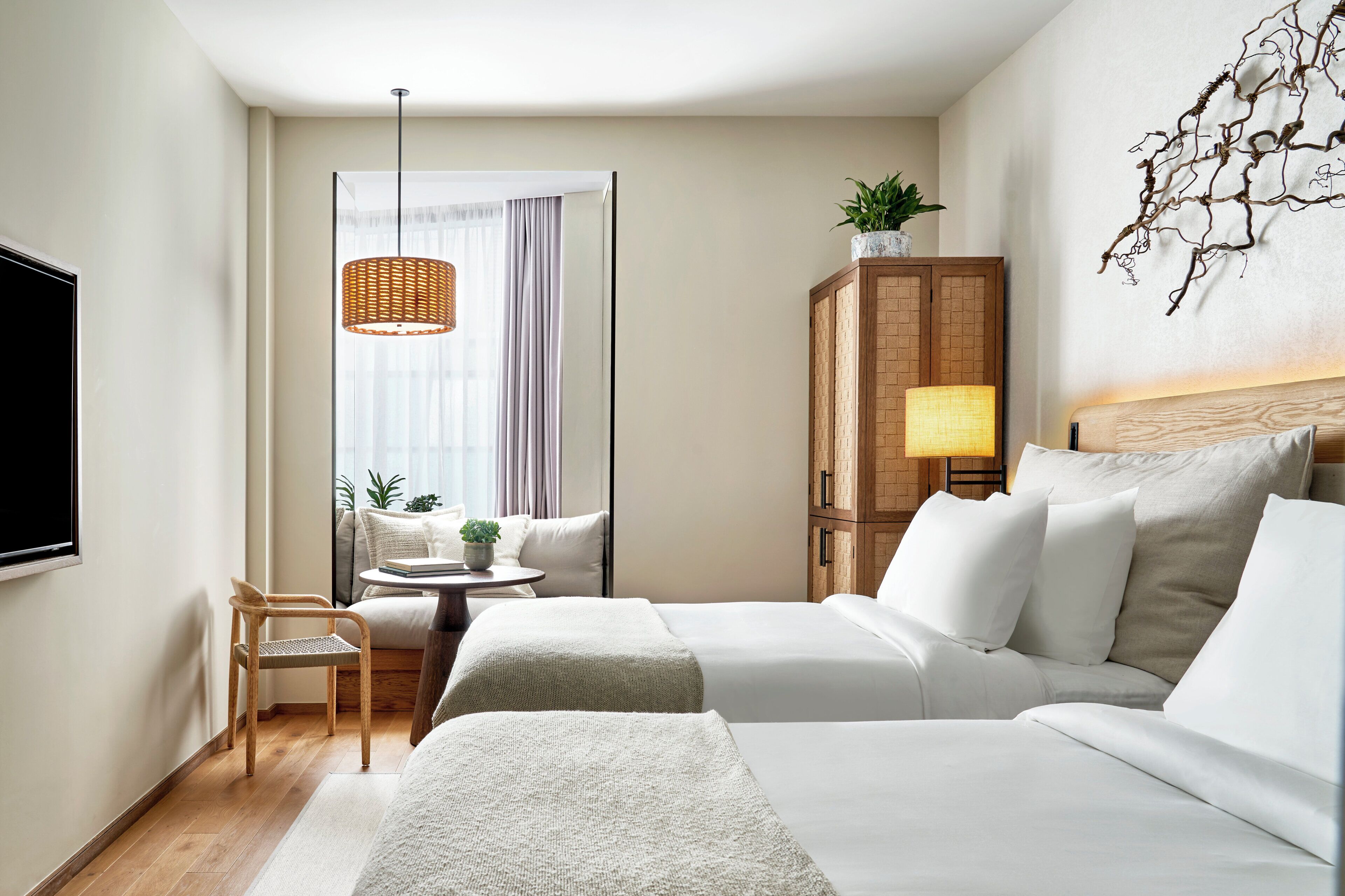 Een hotelkamer met twee bedden, een televisie, een rieten lamp, een houten kast en een plant.