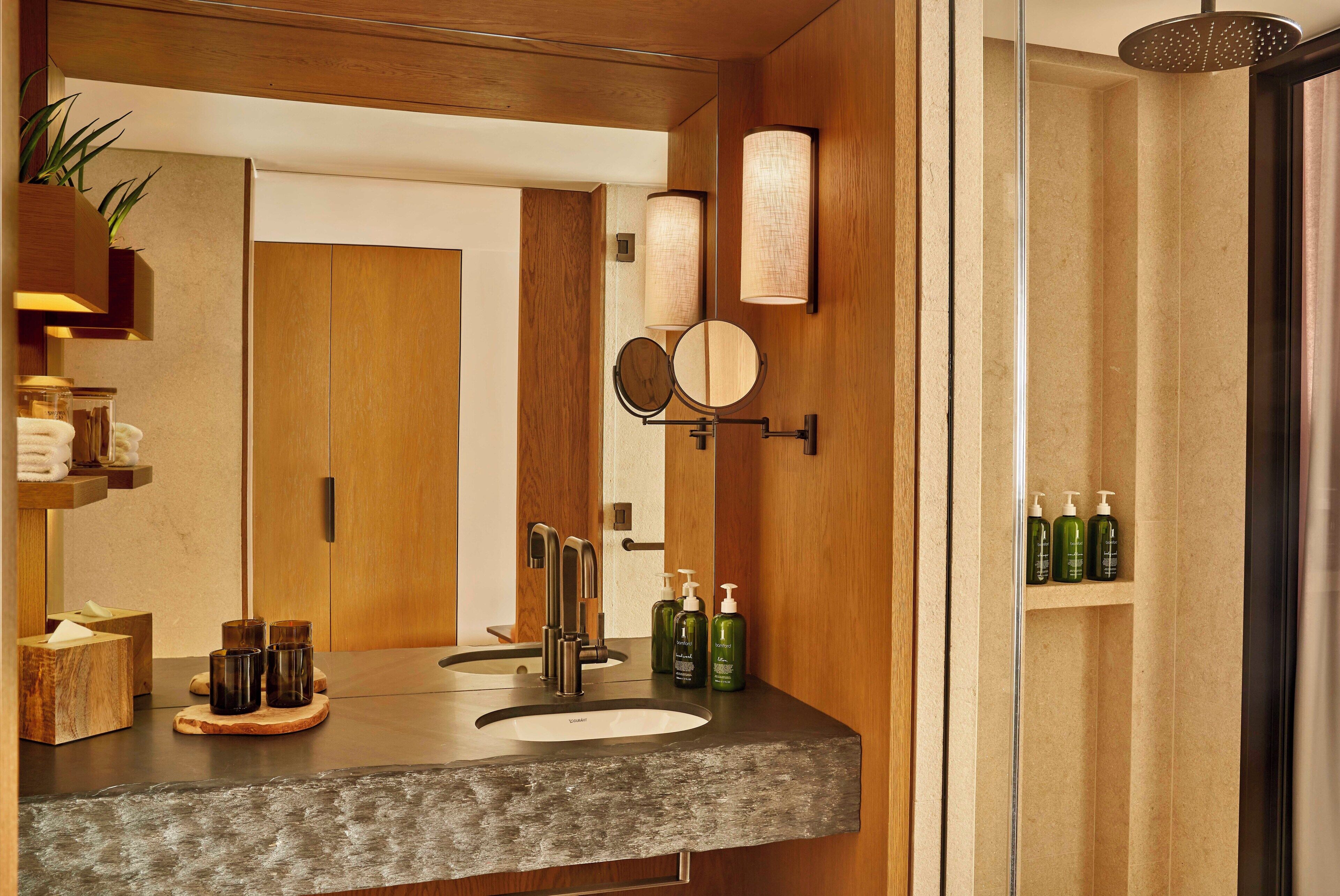A bathroom with a wooden vanity, two sinks, a mirror, and a shower.