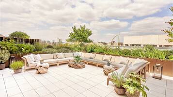 A rooftop patio with a beige sectional sofa, round coffee table, and potted plants.