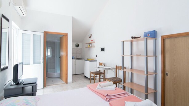 Hotelkamer met een bed, een bureau met computer, een kleine kitchenette, een badkamer en een houten garderobe.
