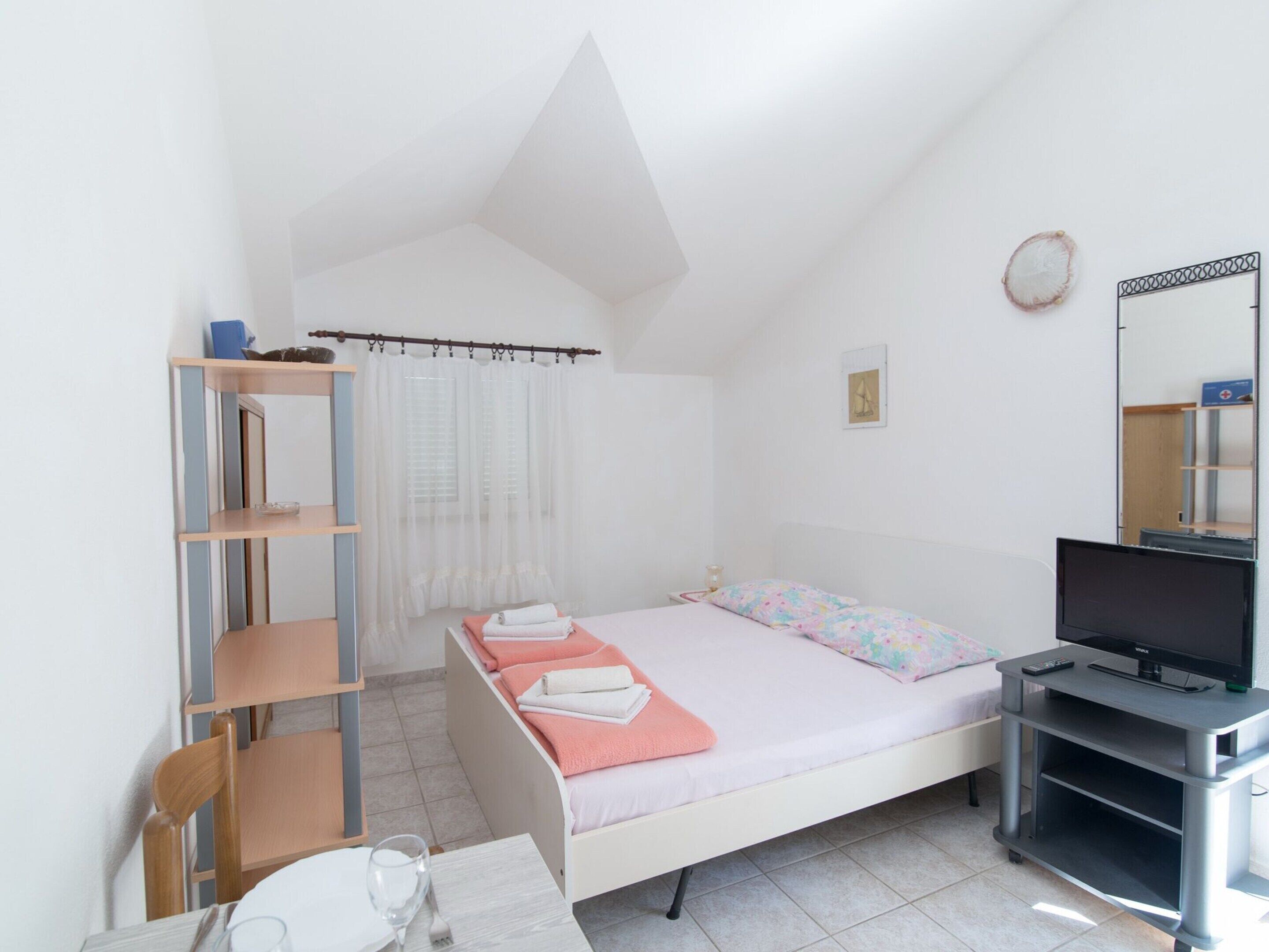 Un dormitorio con cama, televisor, escritorio y silla.