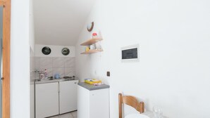 Een compacte keuken met witte kastjes, een kleine koelkast en een eethoek met een houten stoel en tafel.