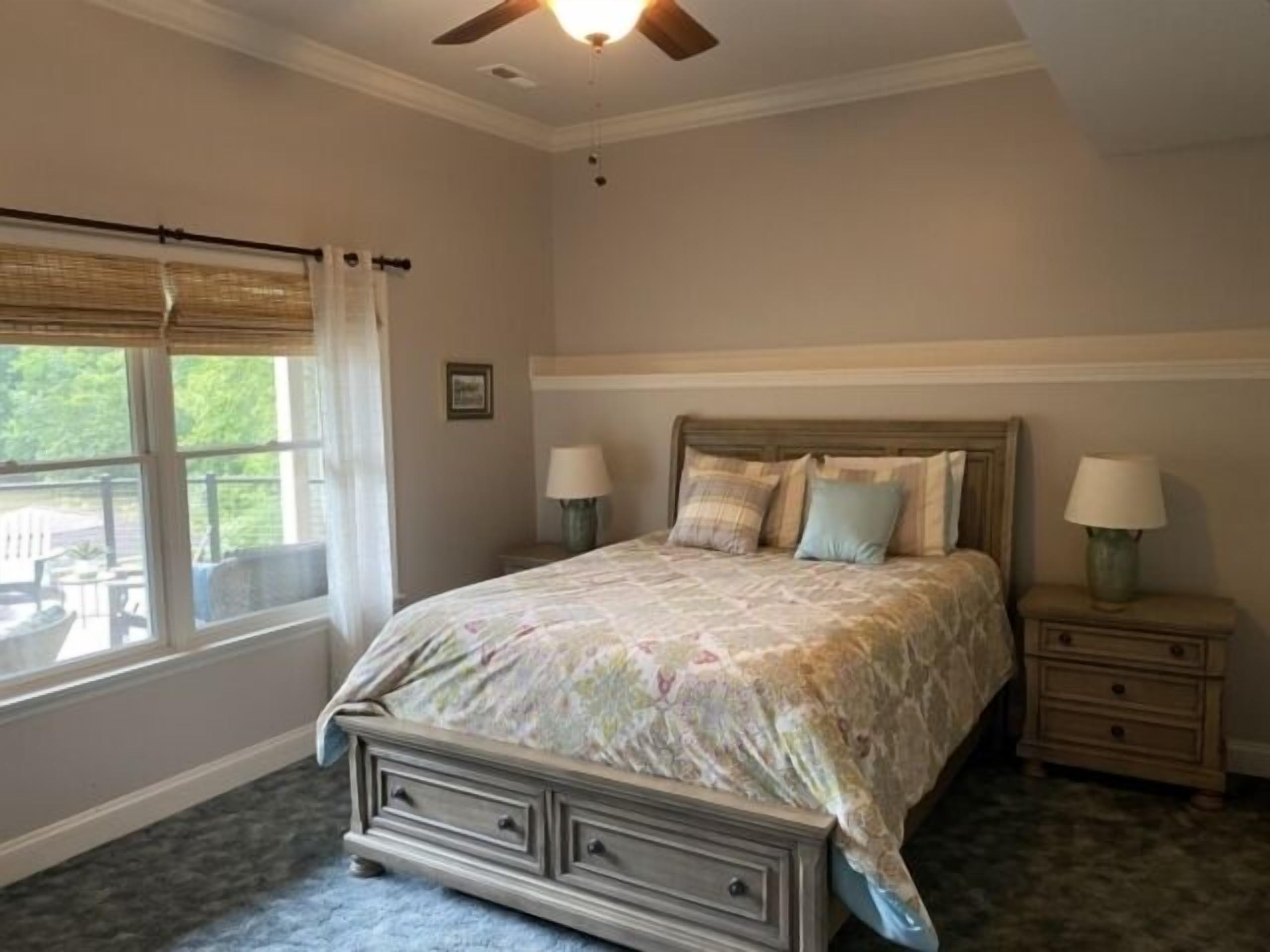A bedroom with a bed, two bedside tables, a ceiling fan, and a window with curtains.