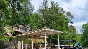 A lakeside property with a dock, a covered seating area, and a house in the background.