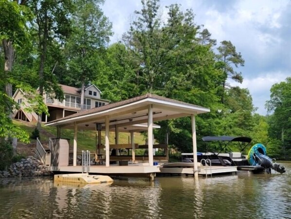 A lakeside property with a dock, a covered seating area, and a house in the background.