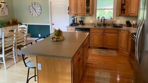 A kitchen with wooden cabinets, a central island, a clock, and a window.