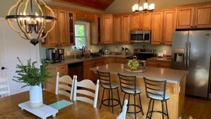 A kitchen with wooden cabinets, a stainless steel refrigerator, a central island with bar stools, and pendant lighting.