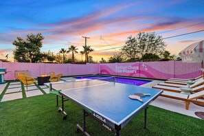 Tischtennisplatte, Stühle und Billardtisch in einer Außenanlage mit Sonnenuntergangshimmel.