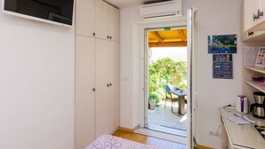 A compact room with a bed, a wardrobe, a kitchenette, and an open door leading to a patio with a table and chairs. - Apartments and Room Frane - Double Room (Dubrovnik)