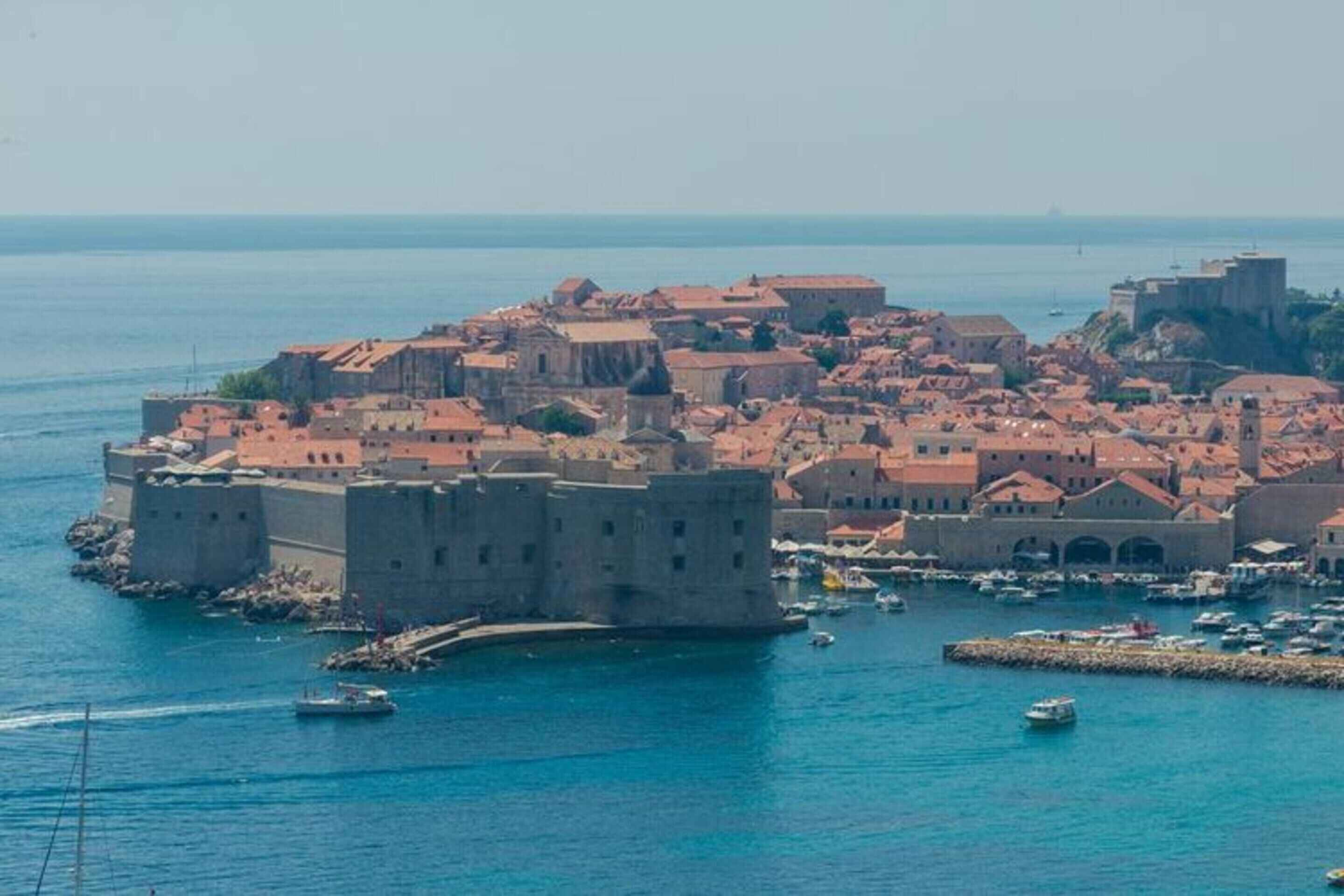 Una ciudad costera con arquitectura histórica, un castillo fortificado y un puerto deportivo con barcos.