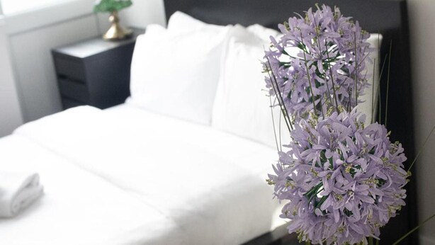 A neatly made bed with white linens, a black headboard, and a vase of purple flowers on the nightstand. - 4 Bedroom-southampton-sleeps 6- Garden (Southampton)