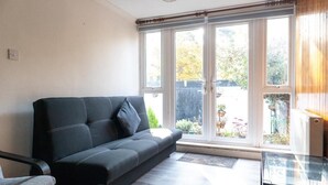 A living room with a black sofa, a glass coffee table, and a view of a garden through large windows. - 4 Bedroom-southampton-sleeps 6- Garden (Southampton)