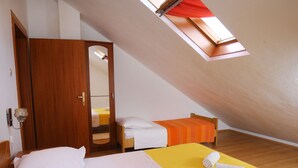 A small, sloped-roofed room with two beds, one with a yellow bedspread and the other with a white bedspread. There is a wooden wardrobe and a small mirror on the wall. - Apartments Boro - Two Bedroom Apartment With Terrace (Supetar)
