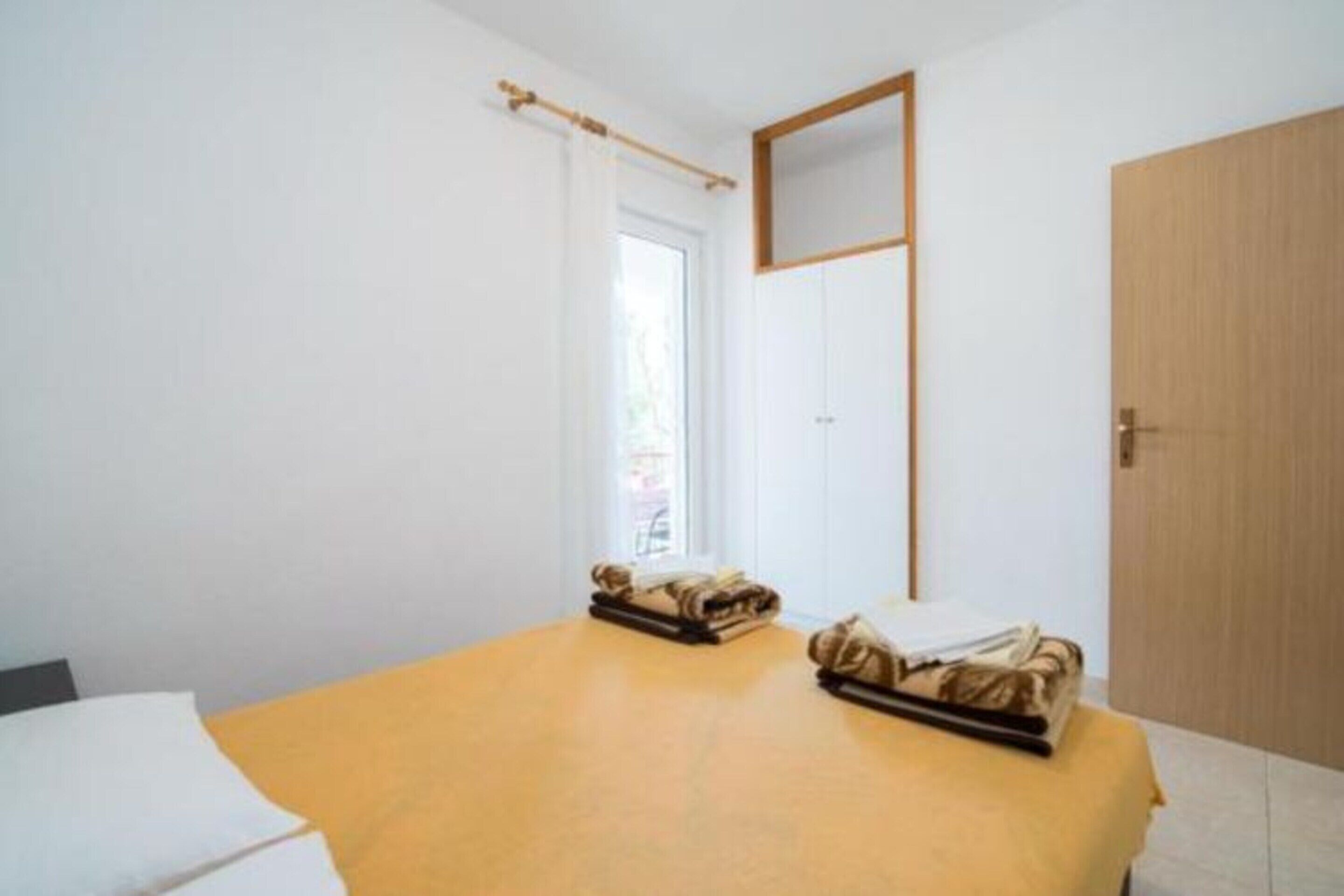 A room with a bed, a wooden door, and a window with a curtain.