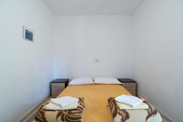Ein schmaler Raum mit einem Einzelbett, zwei Nachttischen und einer kleinen Wandleuchte.