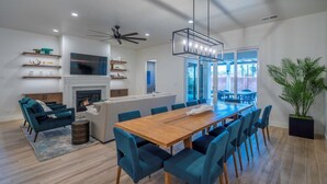 A modern kitchen with a fireplace, a dining area with blue chairs, and a large window overlooking a patio. - Arcadia 64 | Private Hot Tub * Views * Arcade * Pool Table (Santa Clara)