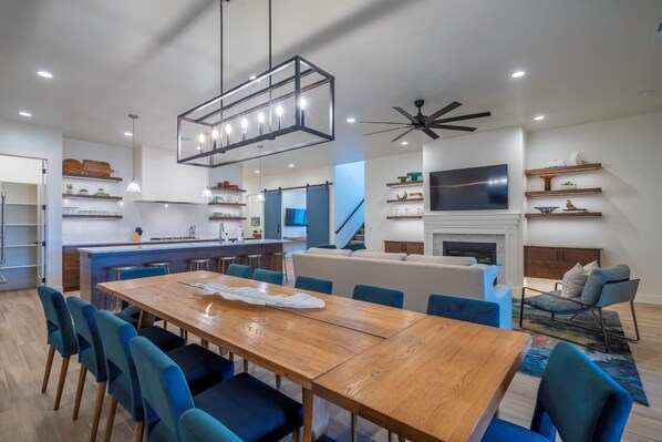 A modern kitchen with a central island, blue chairs, a wooden dining table, and a ceiling fan. - Arcadia 64 | Private Hot Tub * Views * Arcade * Pool Table (Santa Clara)