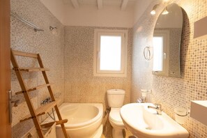 Ein Badezimmer mit Mosaikfliesen, einer Holzleiter, einer Badewanne, einer Toilette und einem Waschbecken.
