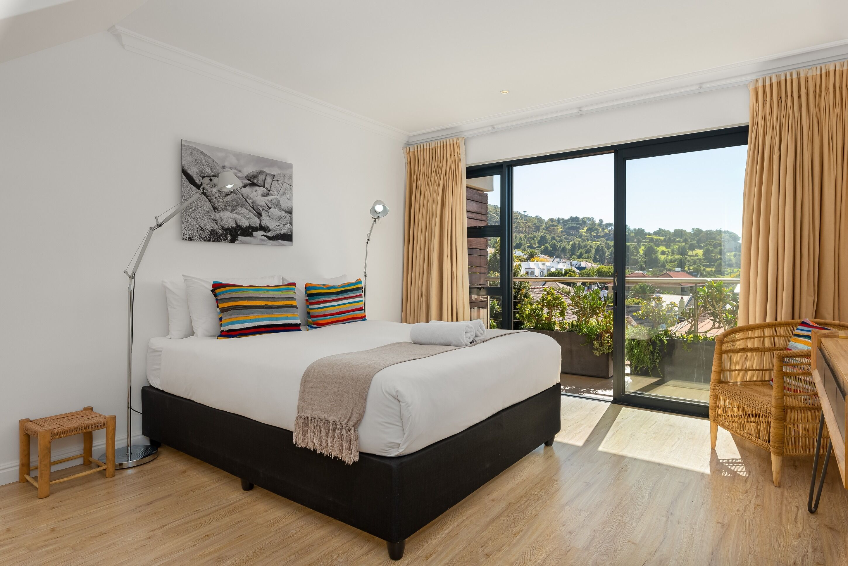 Een moderne slaapkamer met een groot bed, uitzicht op de natuur en een balkon met rieten meubels.