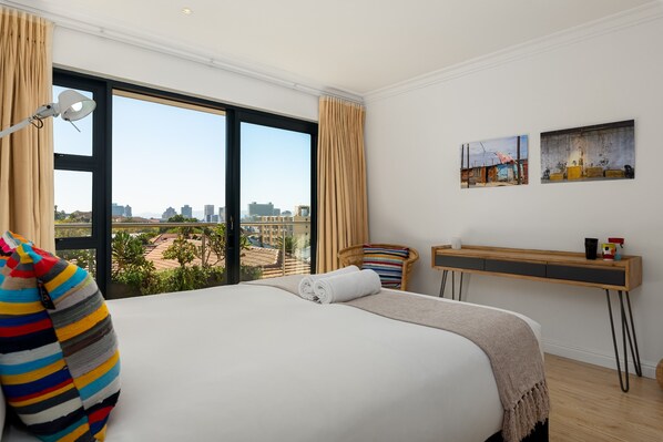Un cuarto de hotel con una cama grande, un escritorio y vista a la ciudad.