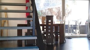 Un intérieur moderne avec un escalier menant à un niveau supérieur, un coin repas avec des chaises et une table, et une vue dégagée sur l’extérieur grâce à une grande fenêtre.