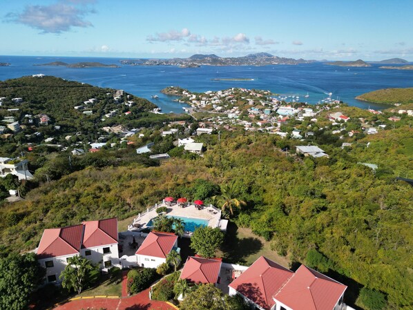 Vue aérienne d’une zone côtière avec des immeubles résidentiels, une piscine et une vue sur la mer et les îles au loin.