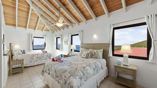 A bedroom with a large bed, two bedside tables, a ceiling fan, and a window with a view. - 2 bedroom, 2.5 bath with pool access & ocean view (Cruz Bay)