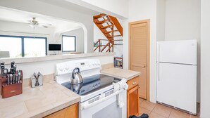 A kitchen with a stove, kettle, and refrigerator, wooden staircase, and a window with blinds. - 2 Bedroom Villa with Pool & Panoramic Views (Cruz Bay)