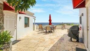 A patio with a table and chairs, a red umbrella, and a view of the sea. - 2 Bedroom Villa with Pool & Panoramic Views (Cruz Bay)