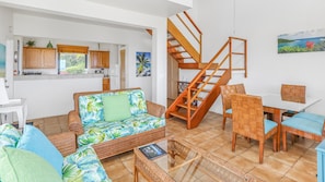 A living room with a sofa, chairs, a dining table, and a staircase.