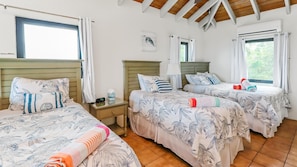 Une chambre d’hôtel avec trois lits, chacun recouvert d’une couvre-lit à motifs floraux, une table de chevet avec une horloge et une fenêtre avec des rideaux.