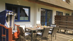 Una terraza de madera con una mesa y sillas, un espacio de descanso cubierto y una valla de madera.