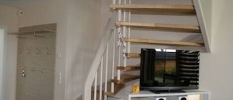 A staircase with wooden steps and a white railing, leading to a landing with a television on a white stand.