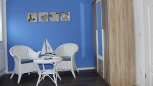 Una habitación con una pared azul, dos sillas blancas, una mesita pequeña y una maqueta de un velero.