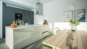 Een moderne keuken met een centraal eiland, geïntegreerde apparatuur en een eethoek met een houten tafel en groene stoelen.