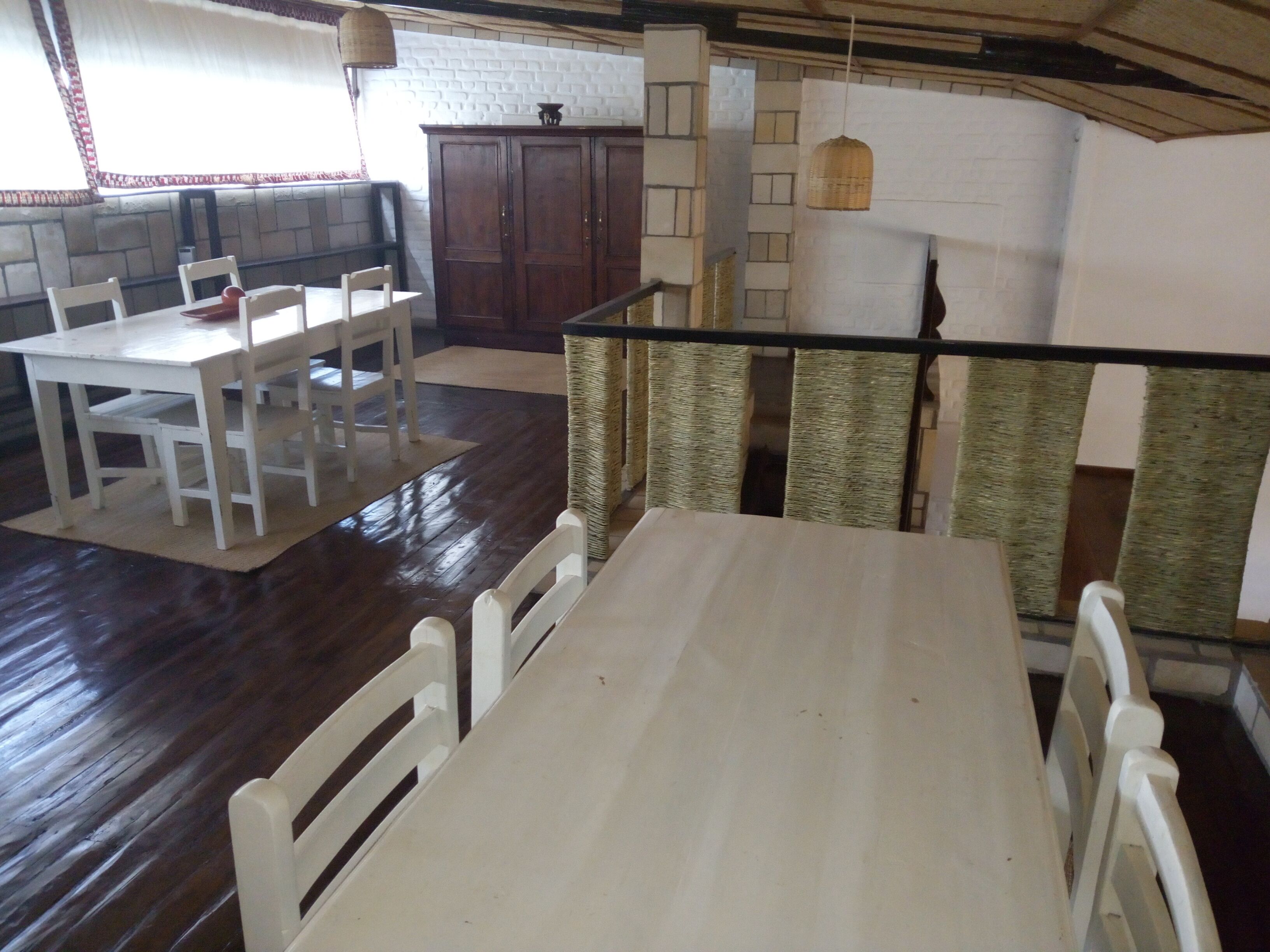 A dining area with a white table and chairs, a wooden cabinet, and a brick wall.