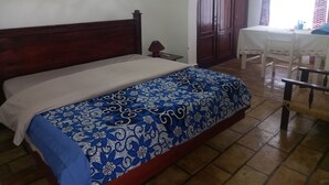 A bedroom with a wooden bed, a small bedside table, a wardrobe, and a dining area with a table and chairs.