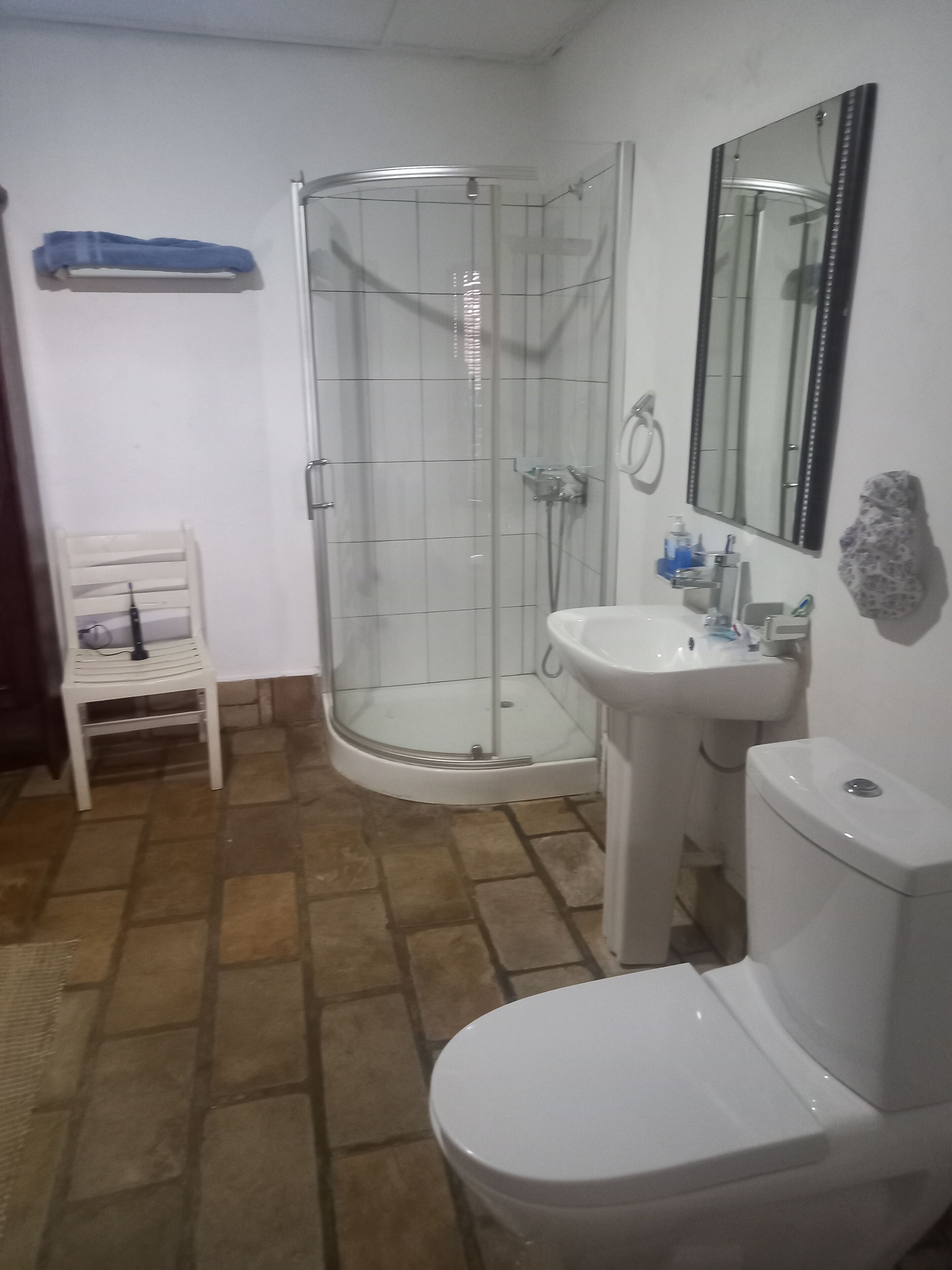 Un baño con cabina de ducha de vidrio, un lavamanos blanco, un inodoro y una silla.