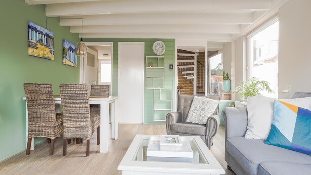 A living room with a sofa, a coffee table, wicker chairs, a bookshelf, and a staircase. - Vacation Home 450 m From the Beach (Katwijk Aan Zee)